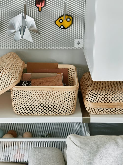 A woven bamboo SMARRA box with lid is on a shelf by a matching box in another size. Its lid is off and notebooks are inside.