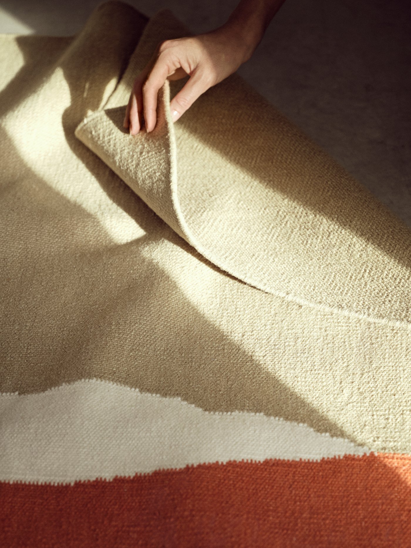 The TVINGSTRUP rug is set on the floor as a hand reaches out to fold a corner of the rug.