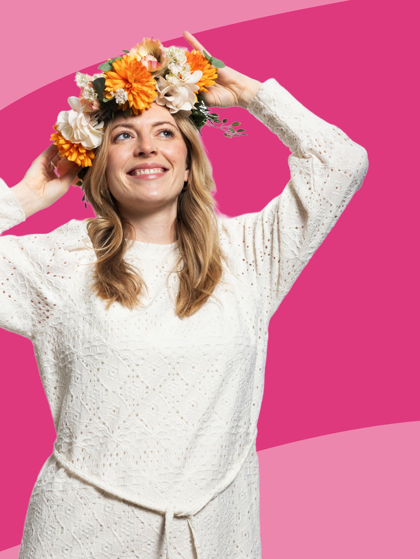 Una donna sorride toccandosi la testa con le mani e indossa una corona di fiori. Sullo sfondo una grafica rosa