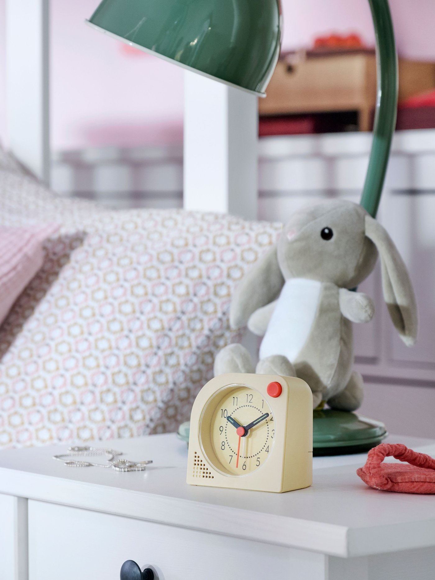 Närbild av HEMNES sängbord med TJINGA väckarklocka, DVÄRGHARE mjukdjur kanin och RÖDFLIK skrivbordslampa.