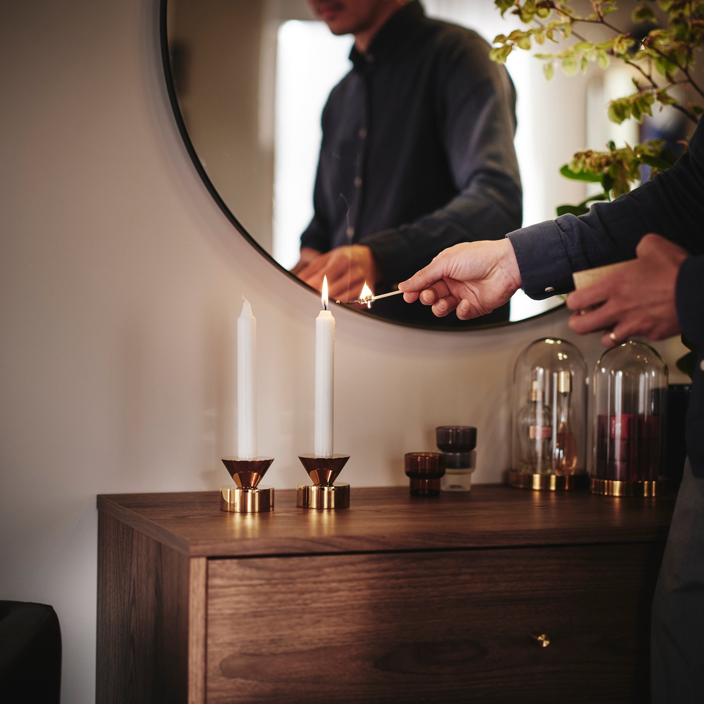 Una persona sta accendendo le candele nei portacandele STOCKHOLM 2025, posizionati sopra una cassettiera RÅDMANSÖ.