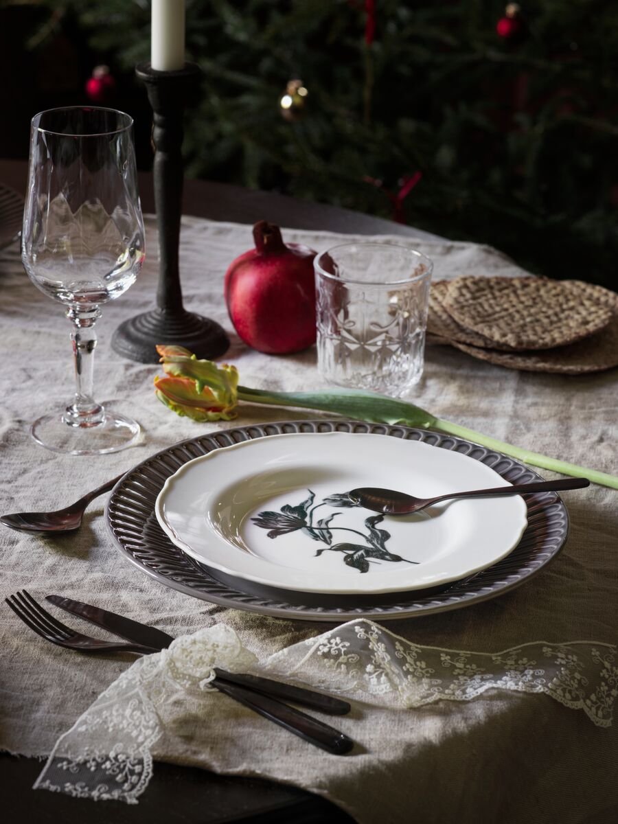 Een traditioneel gedekte tafel, met een wit UPPLAGA bord in het midden bovenop een blauw bord.