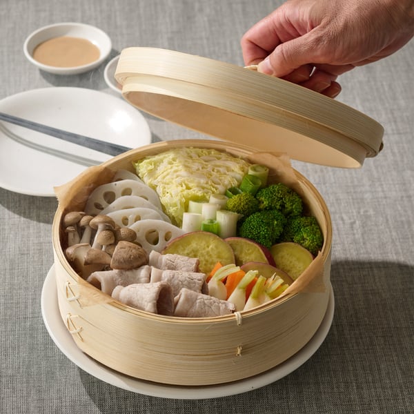 A person lifting the lid on the KLOCKREN steamer, and a cloud of steam reveals a delicious, freshly cooked meal.