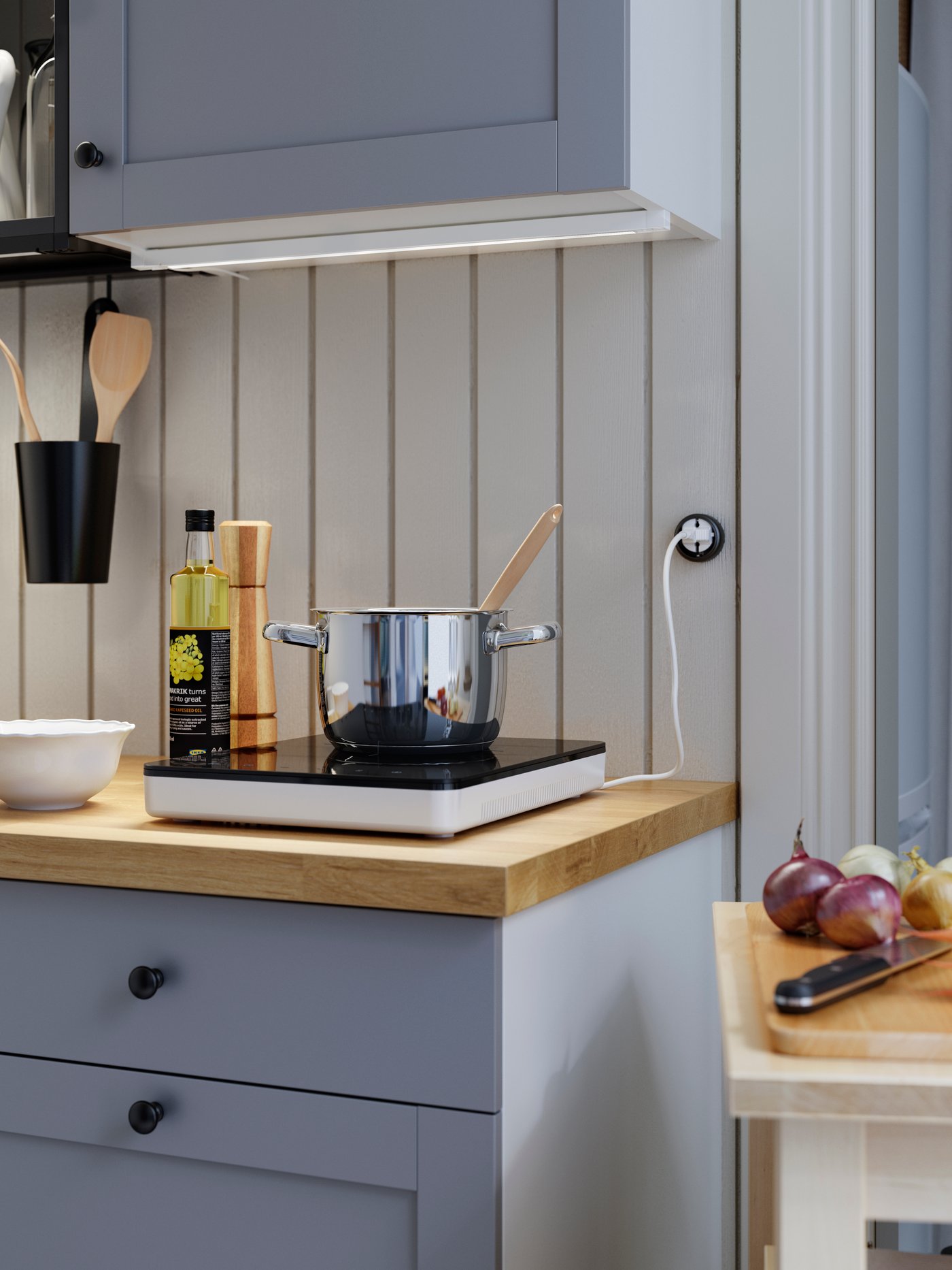 A stainless steel pot on a portable induction hob, placed on a wooden worktop. Oil and a white bowl are next to it.