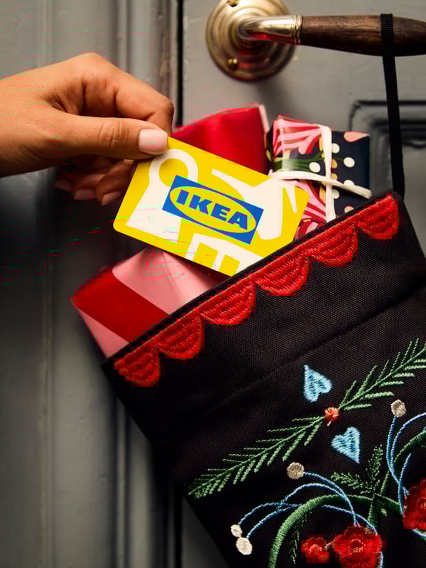 A hand putting an IKEA Gift card in a Christmas stocking hung on a door handle.