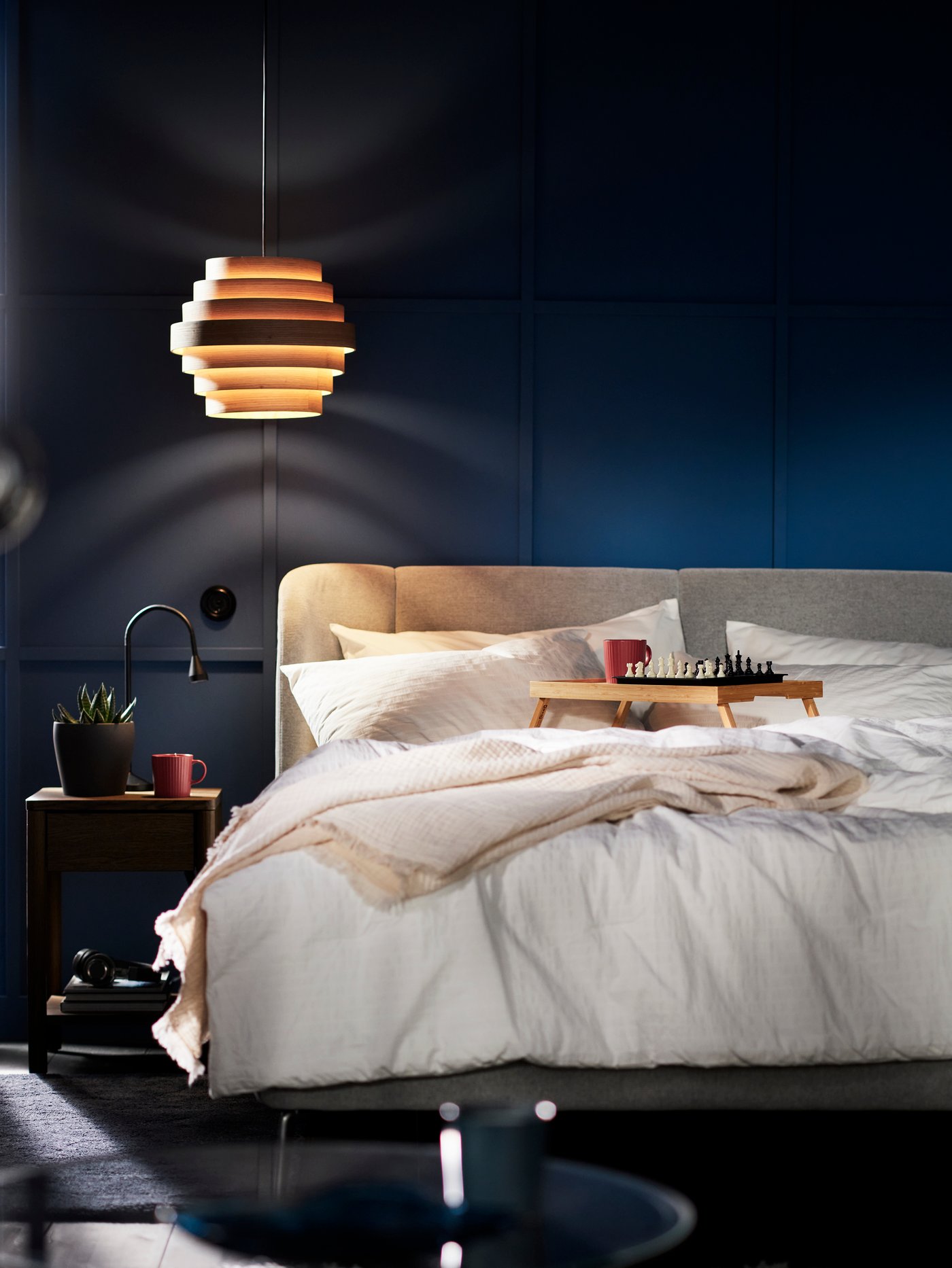 A TUFJORD upholstered bed with a white OFELIA VASS 3 comforter set on it and a DYKARKLOCKA pendant lampshade above.