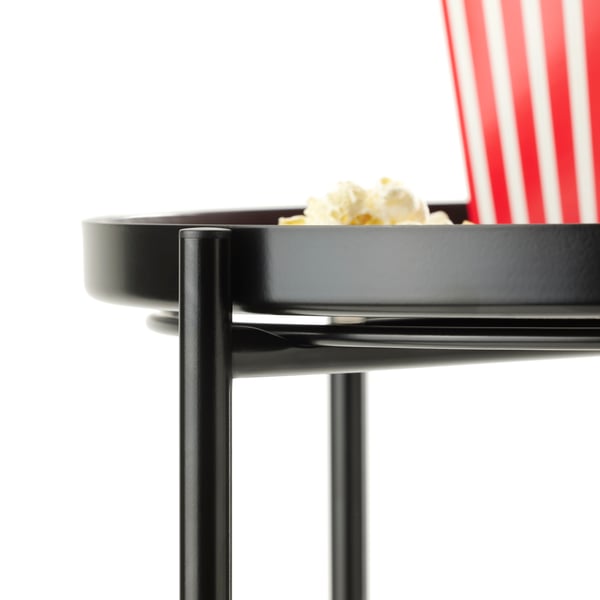 Close-up on the top of a black GLADOM tray table, set into the base. The table is in a white space and holds popcorn.