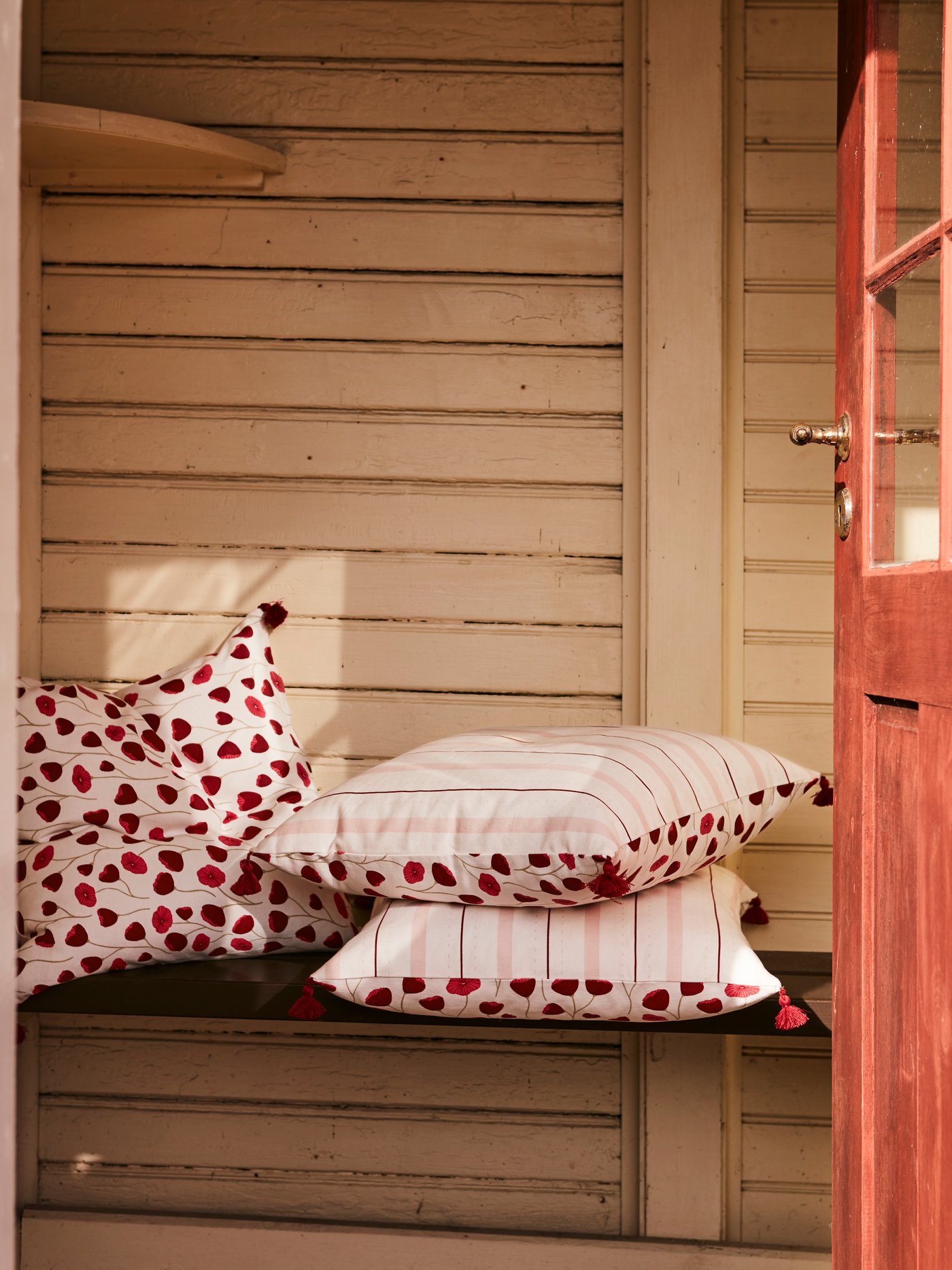ANLEDNING cushion covers with a poppy pattern on one side and stripes on the other placed on a wooden bench.