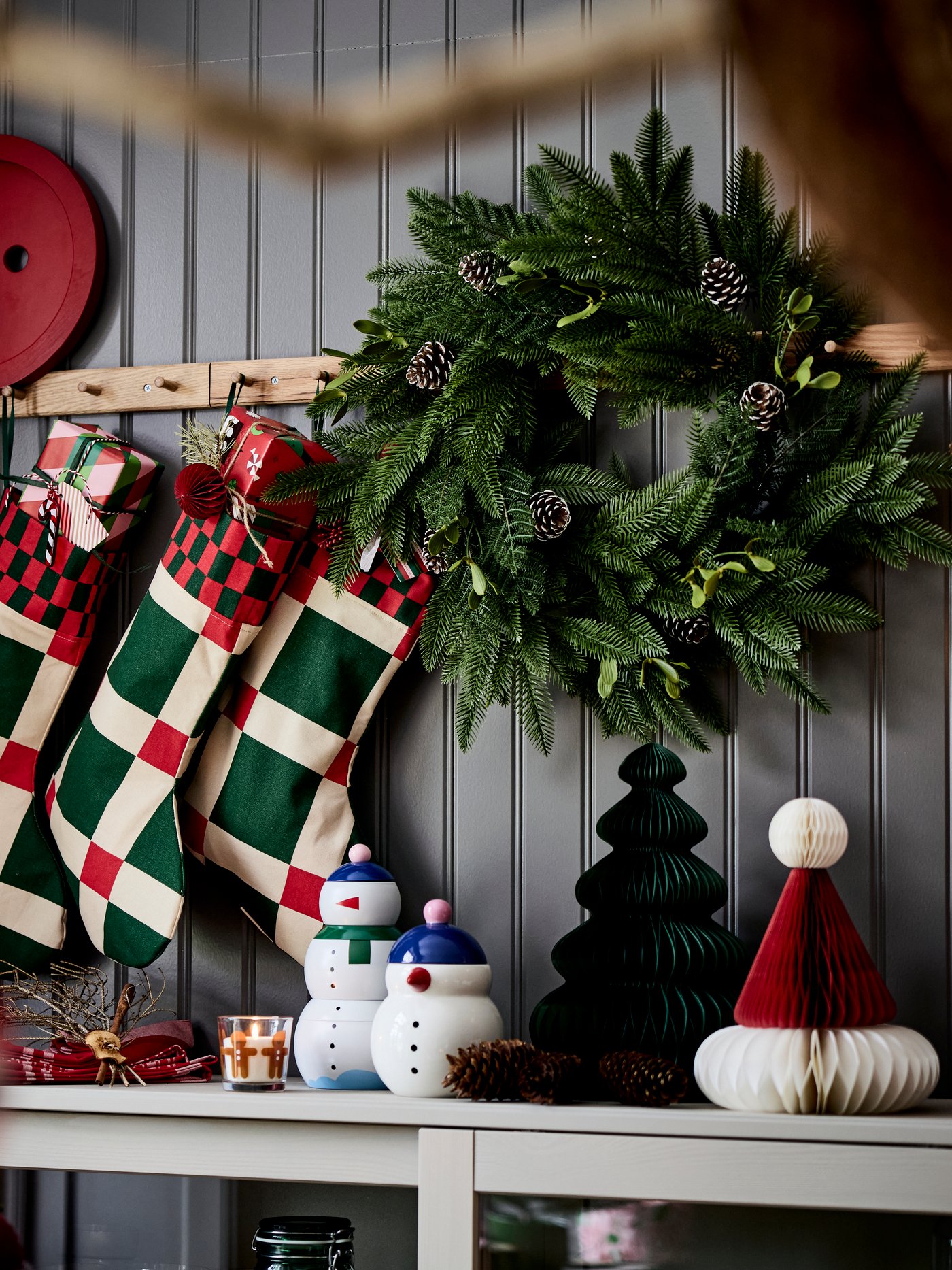 Tre VINTERFINT julstrumpor hänger på krokar med knoppar ovanför ett sideboard med festliga dekorationer.