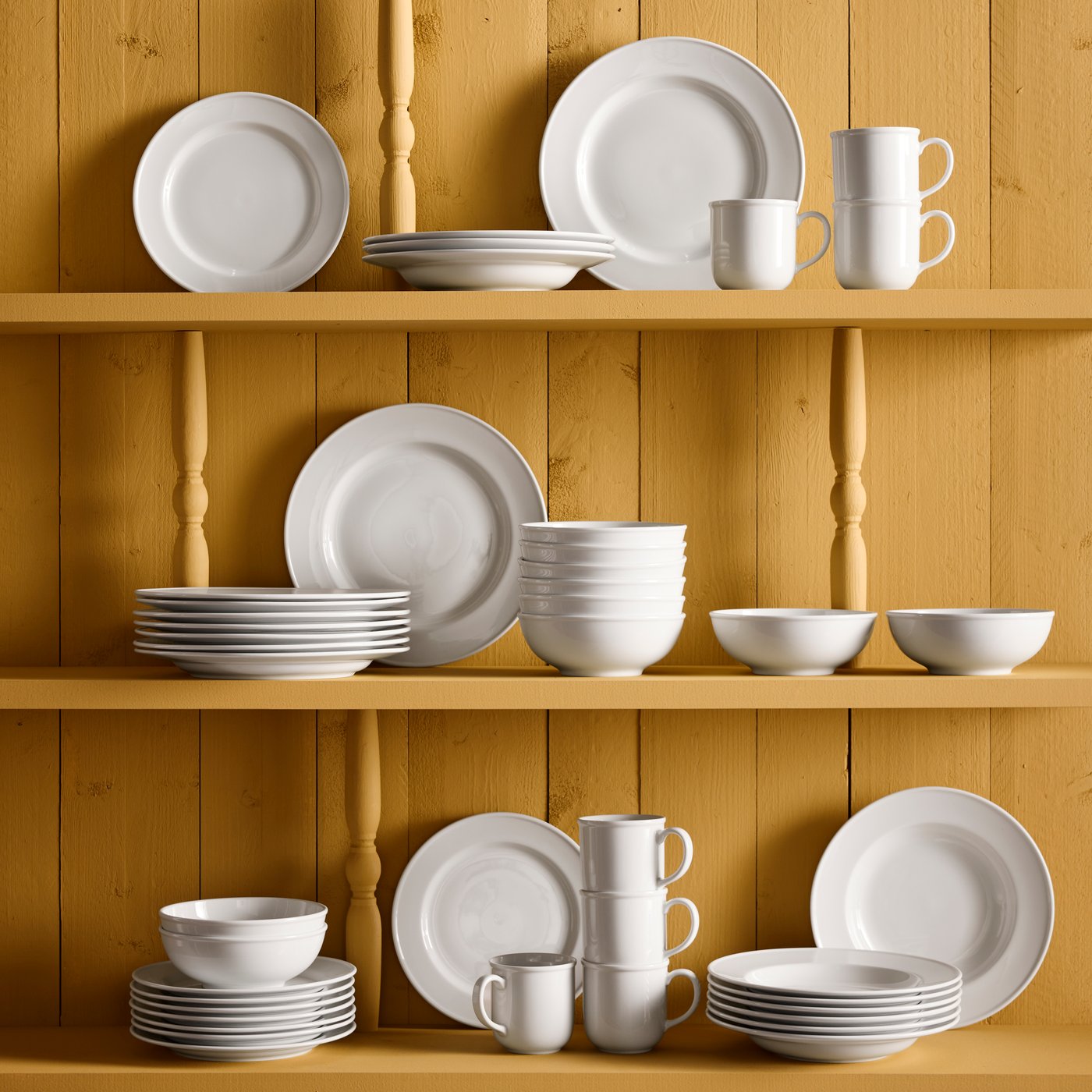 Stacks of VARDAGEN bowls, deep plates, side plates and mugs are on yellow shelves against a yellow wall.