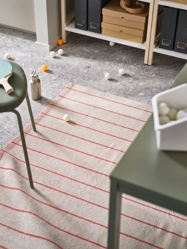 A green VIHALS extendable table stands on a RIDSTIG rug near a shelving unit with some VATTENDRÅG boxes with lid on it.