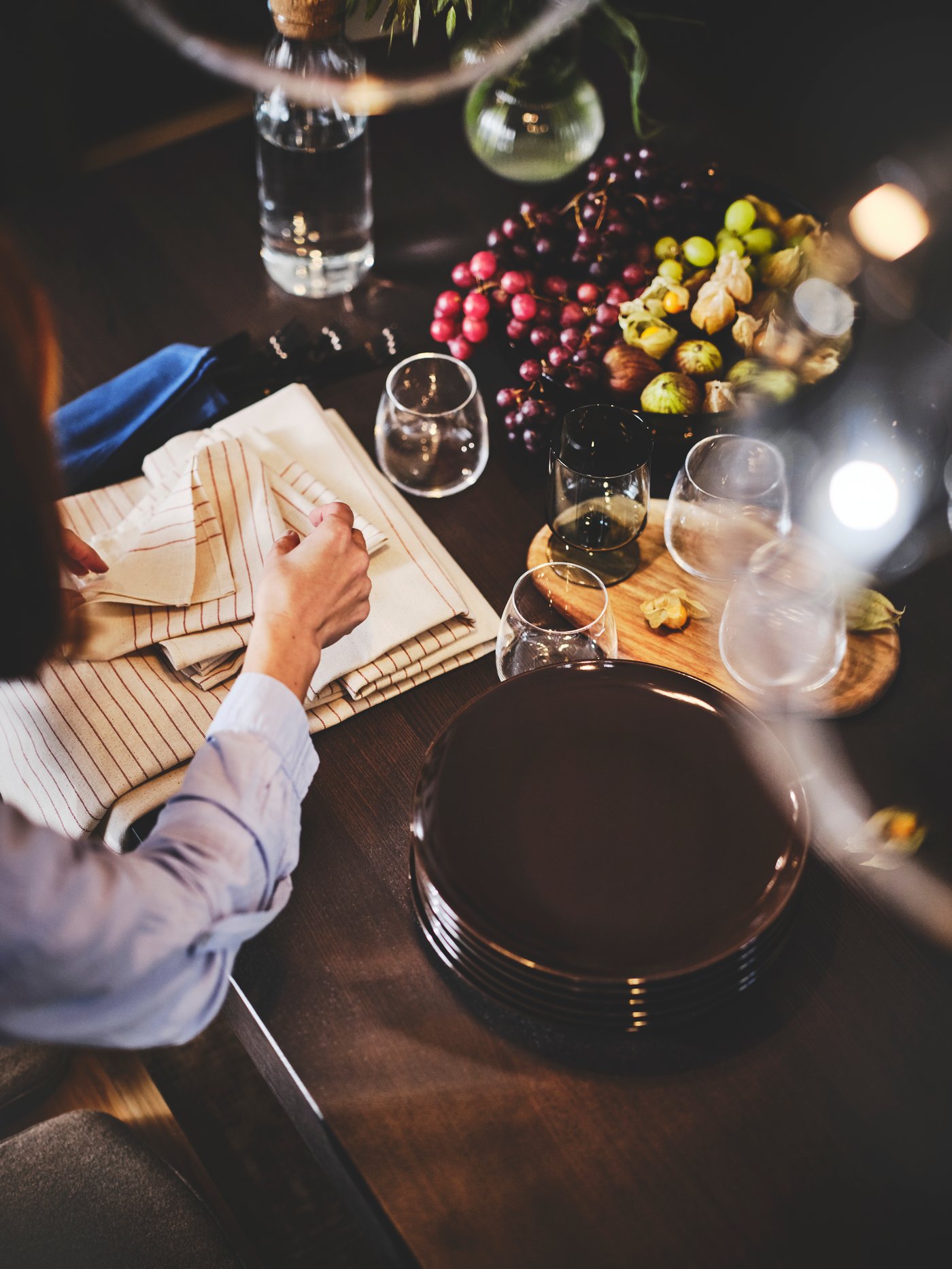 Una persona sentada a una mesa extensible EKEDALEN en una cocina. La mesa tiene servilletas, platos, vasos y una jarra.