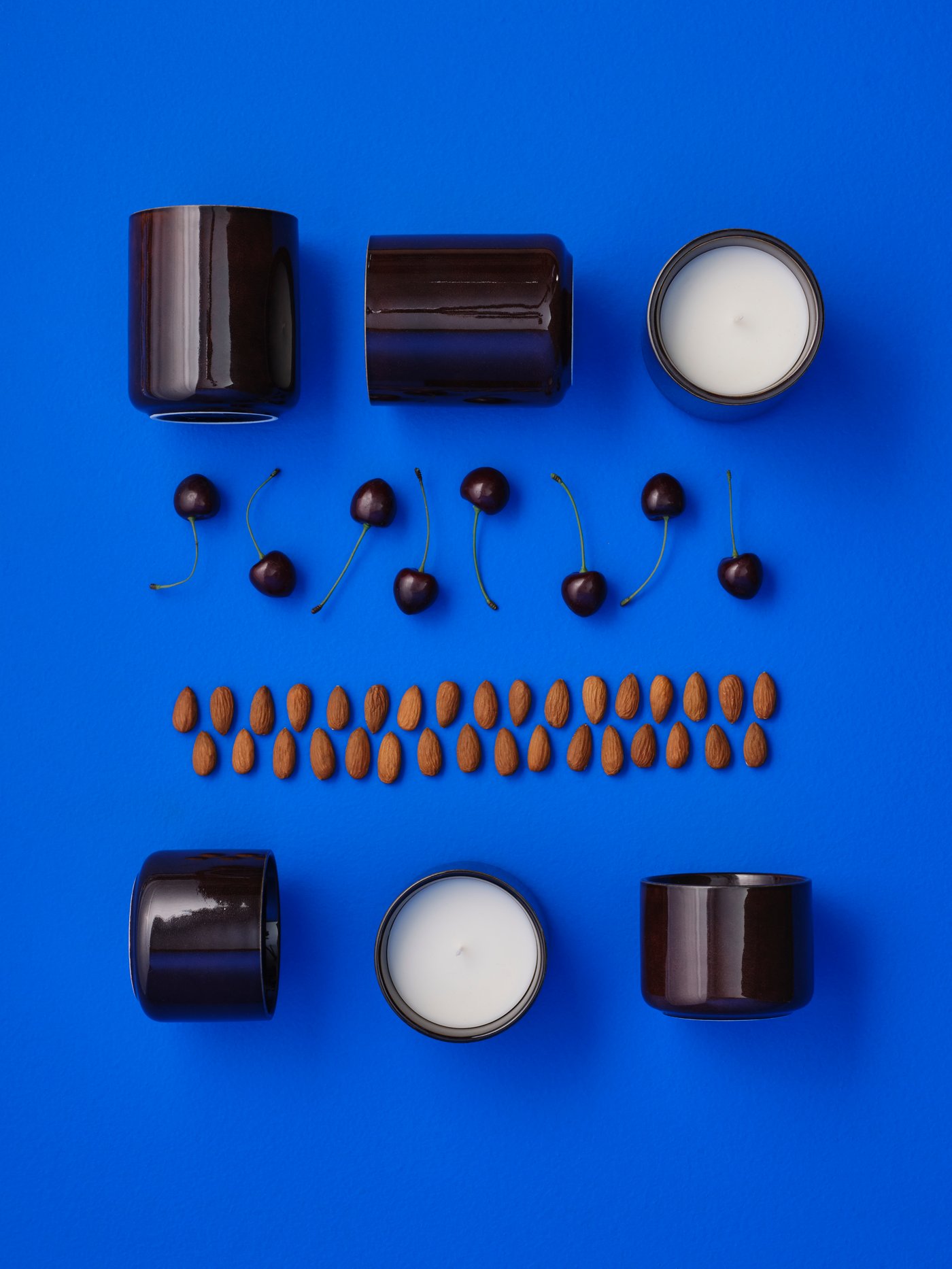 An arrangement of two rows of KOPPARLÖNN almond and cherry scented candles, with almonds and cherries between the rows.