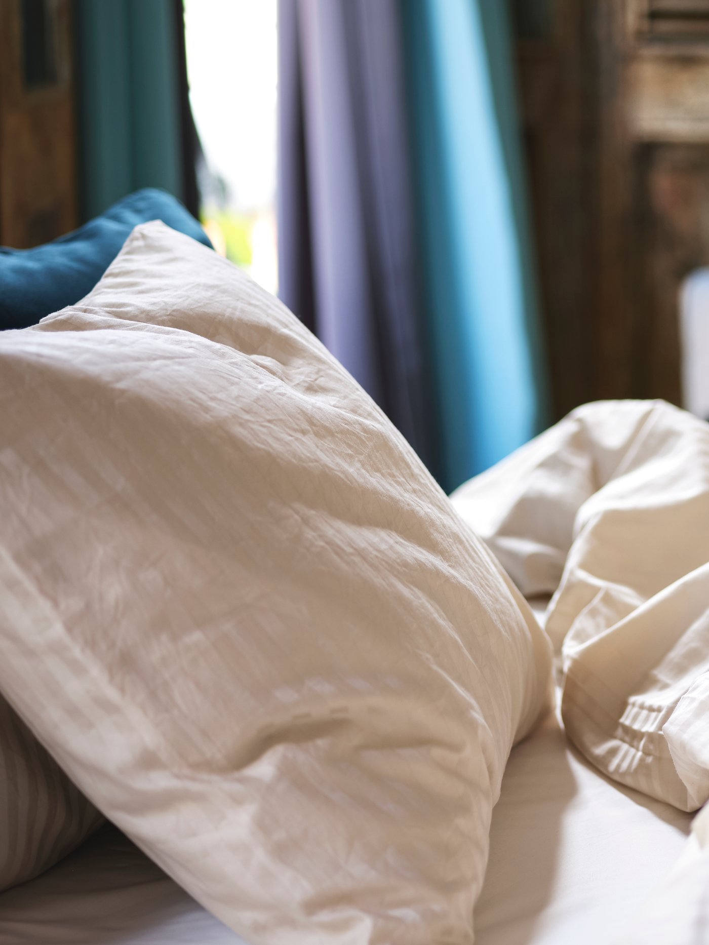 Gros plan sur du linge de lit en satin beige clair placé sur un lit dans une chambre.