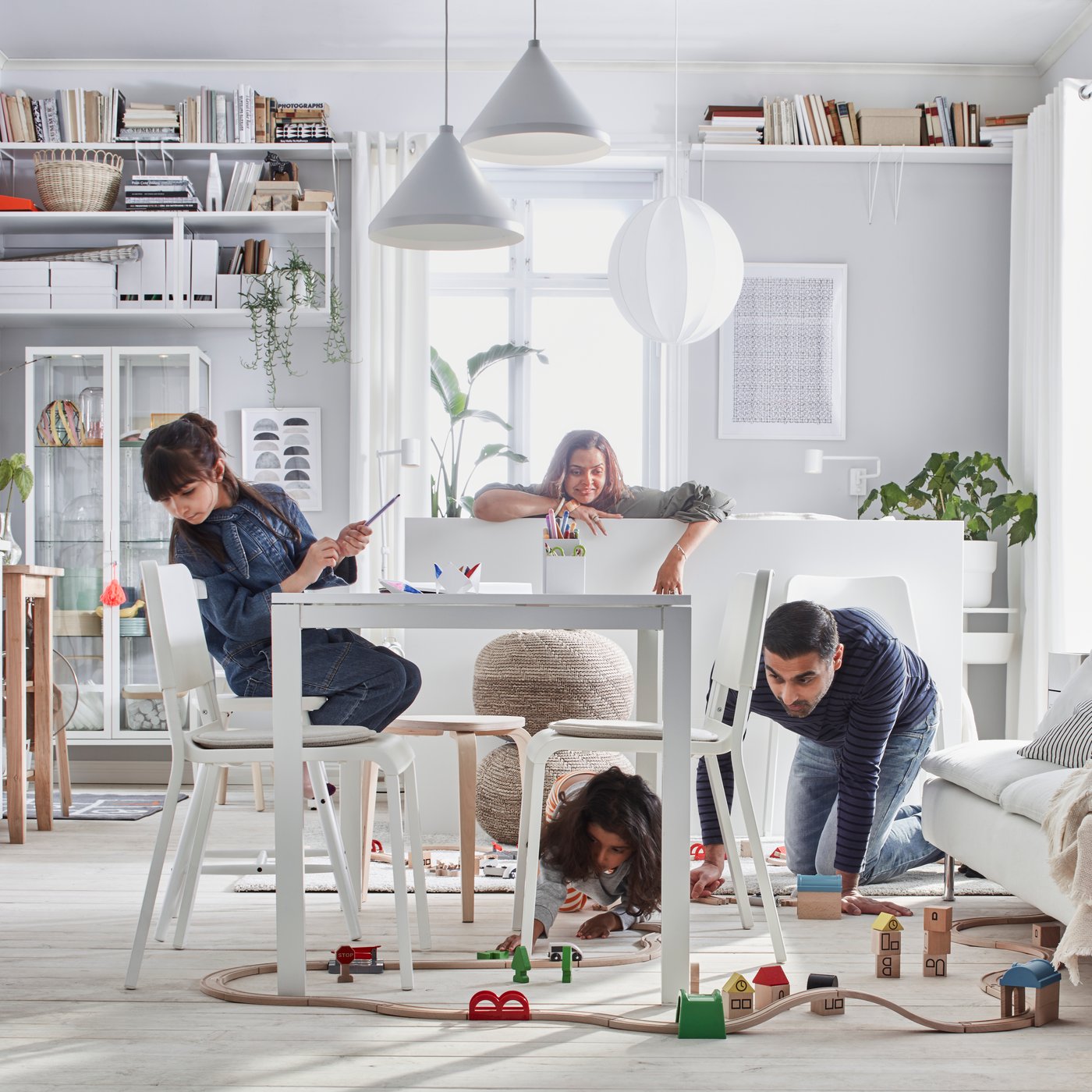 Compact-living home where a family plays with a LILLABO train set in a room with bed, sofa, table, kitchenette, and storage.