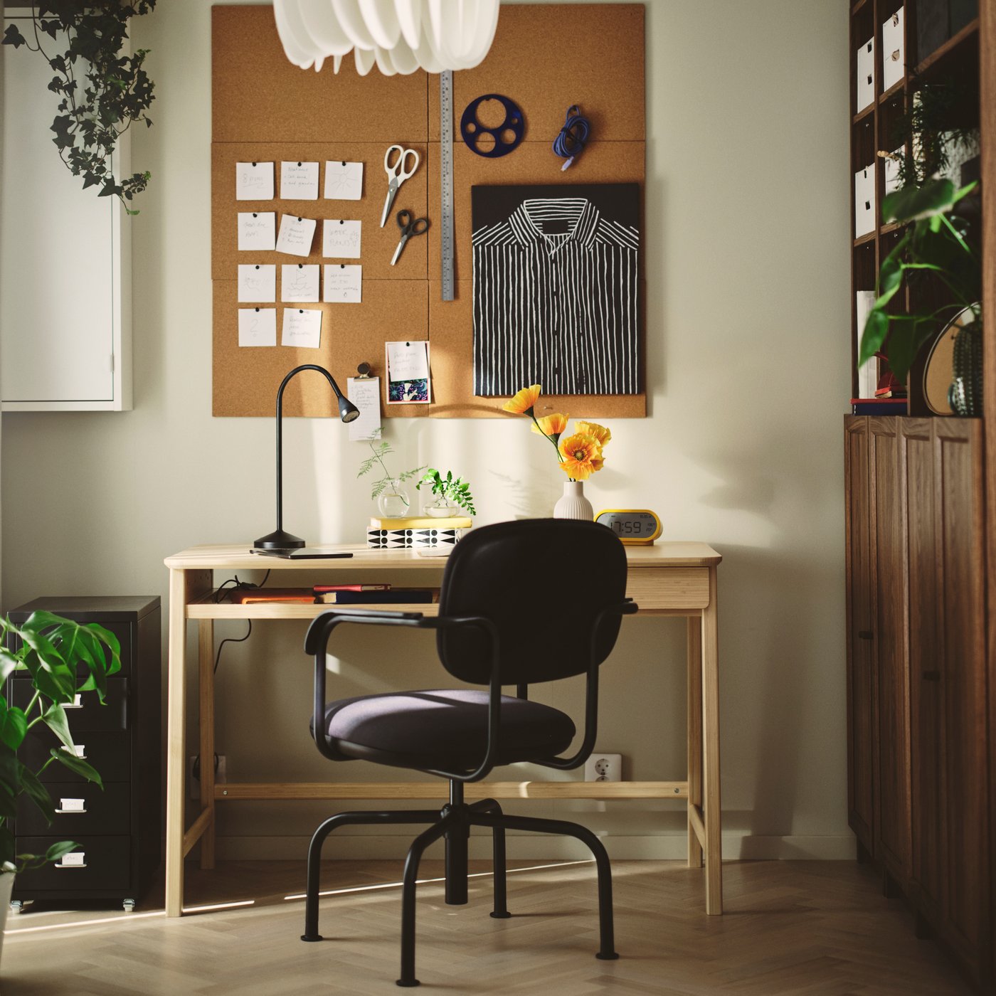 A home office with a dark grey MULLSJÖ swivel chair beside a light wooden desk and a cork board on the wall.