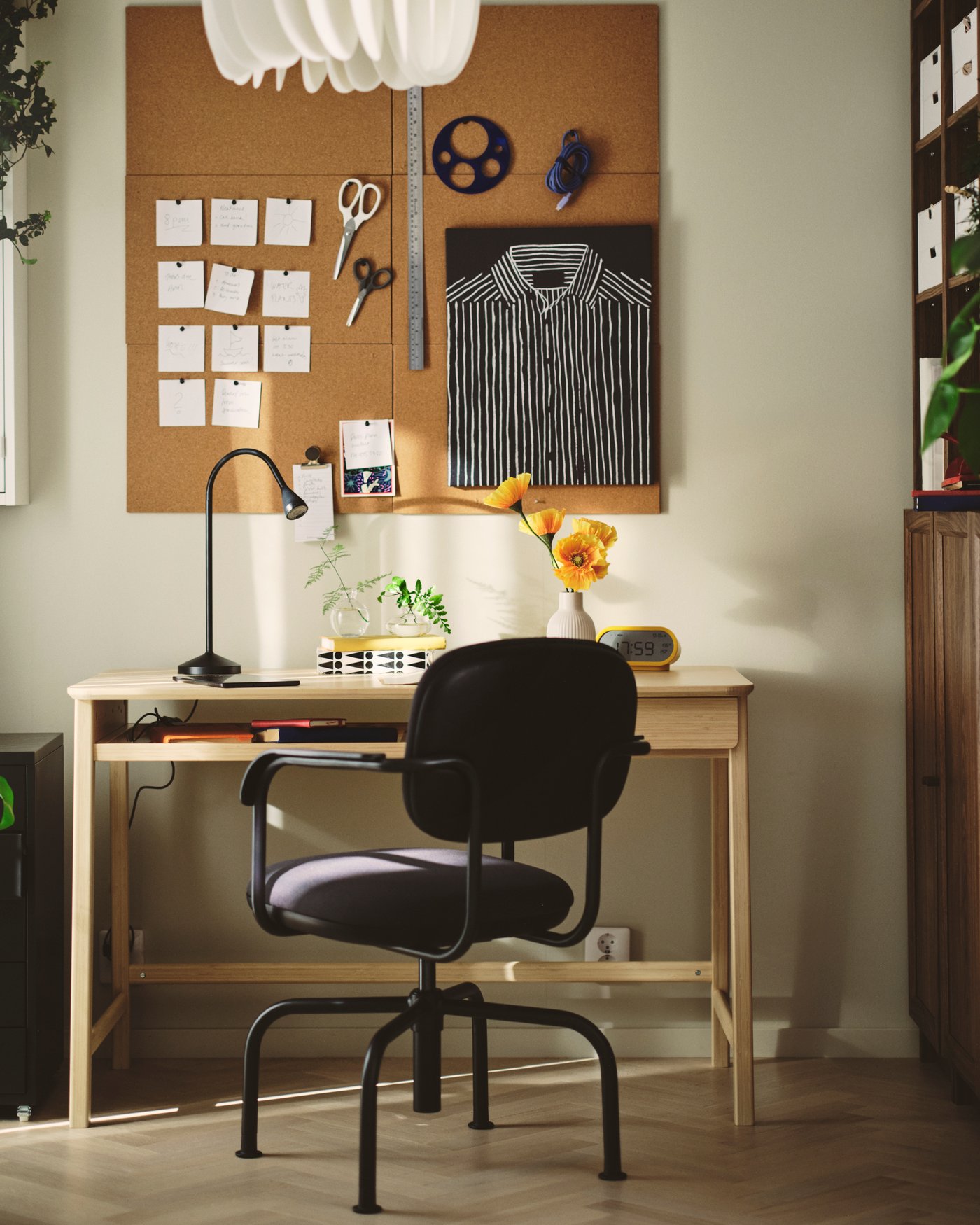 A home office with a dark grey MULLSJÖ swivel chair beside a light wooden desk and a cork board on the wall.