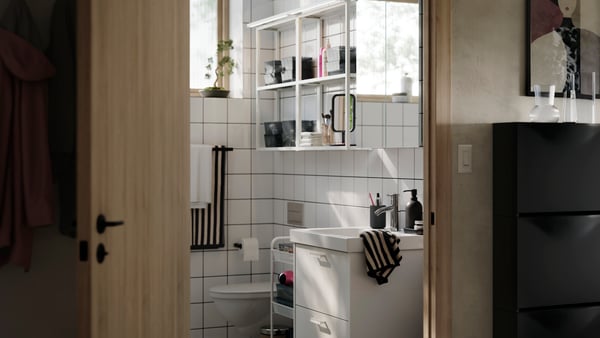 A bright and modern bathroom with white HAVBÄCK storage, white open ENHET shelves on the wall and striped soft towels.