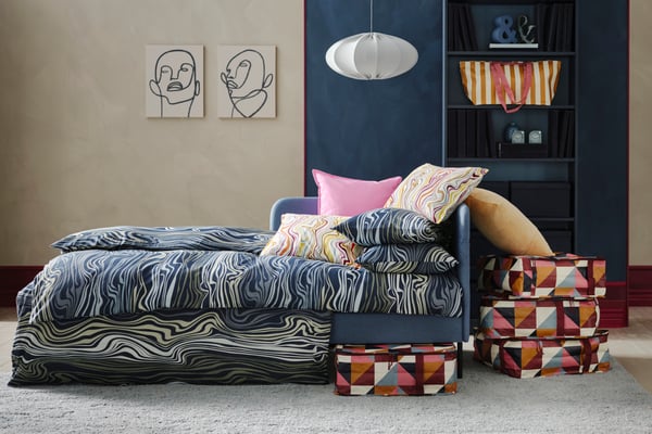 Dormitorio en tonos azules, cama doble con funda nórdica en la misma tonalidad y cojines rosados además de cajas de almacenaje para colocar debajo de la cama con estampados geométricos.