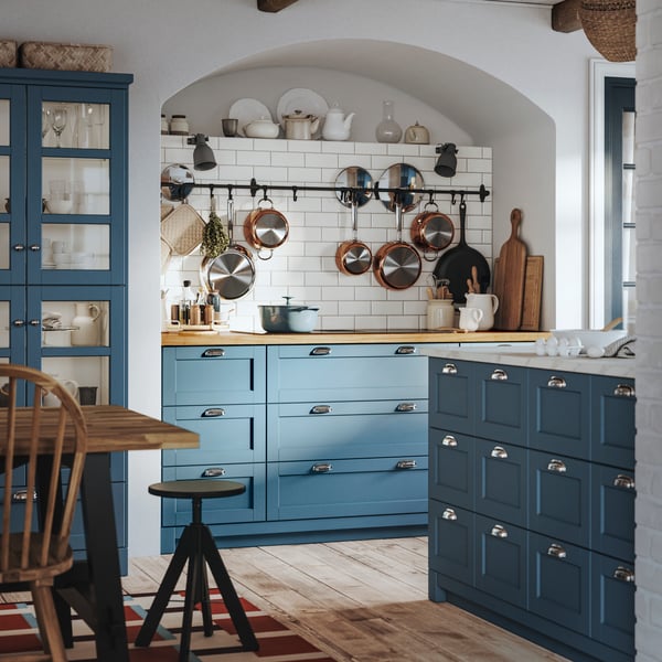 A traditional SEKTION kitchen with blue LERHYTTAN fronts has pots and pans hanging from a wall rail.