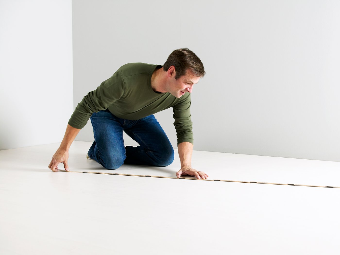 Ein Mann kniet auf einem weißen Boden und misst den Raum mit einem Zollstock aus.