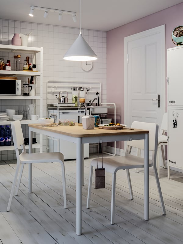 A lunchroom with pink walls and white tiles, a dining table, white chairs, a pendant lamp, a white door.