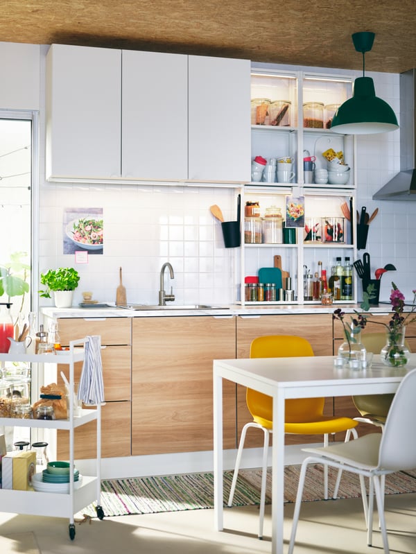 A kitchen with ENHET cabinets, a white MELLTORP table, different-colour LEIFARNE chairs, and a white NISSAFORS trolley.