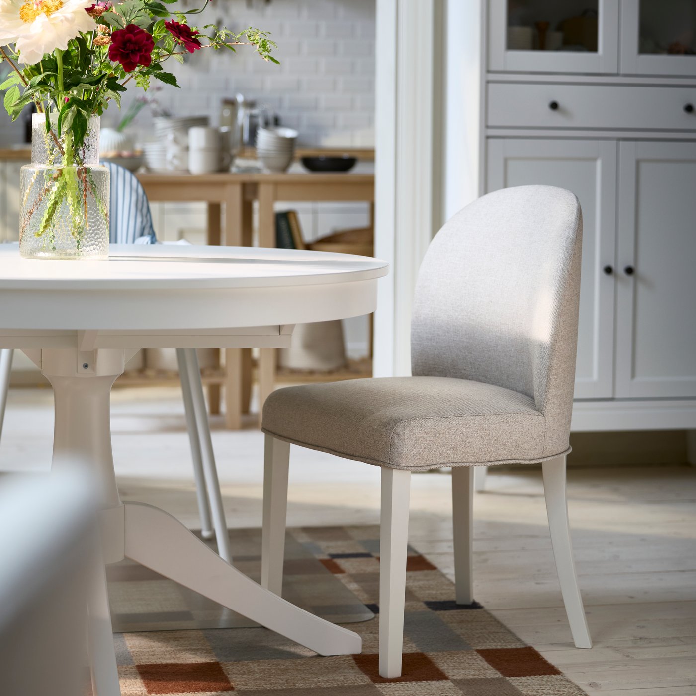 A fully-upholstered ROSENTORP chair in Kilanda light beige/white is placed next to a white ROSENTORP extendable table.
