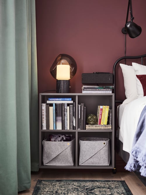 Bedroom with bed frame, cabinet with compartments, bookshelf speaker with WiFi, table lamp, rug, curtains, wall lamp.