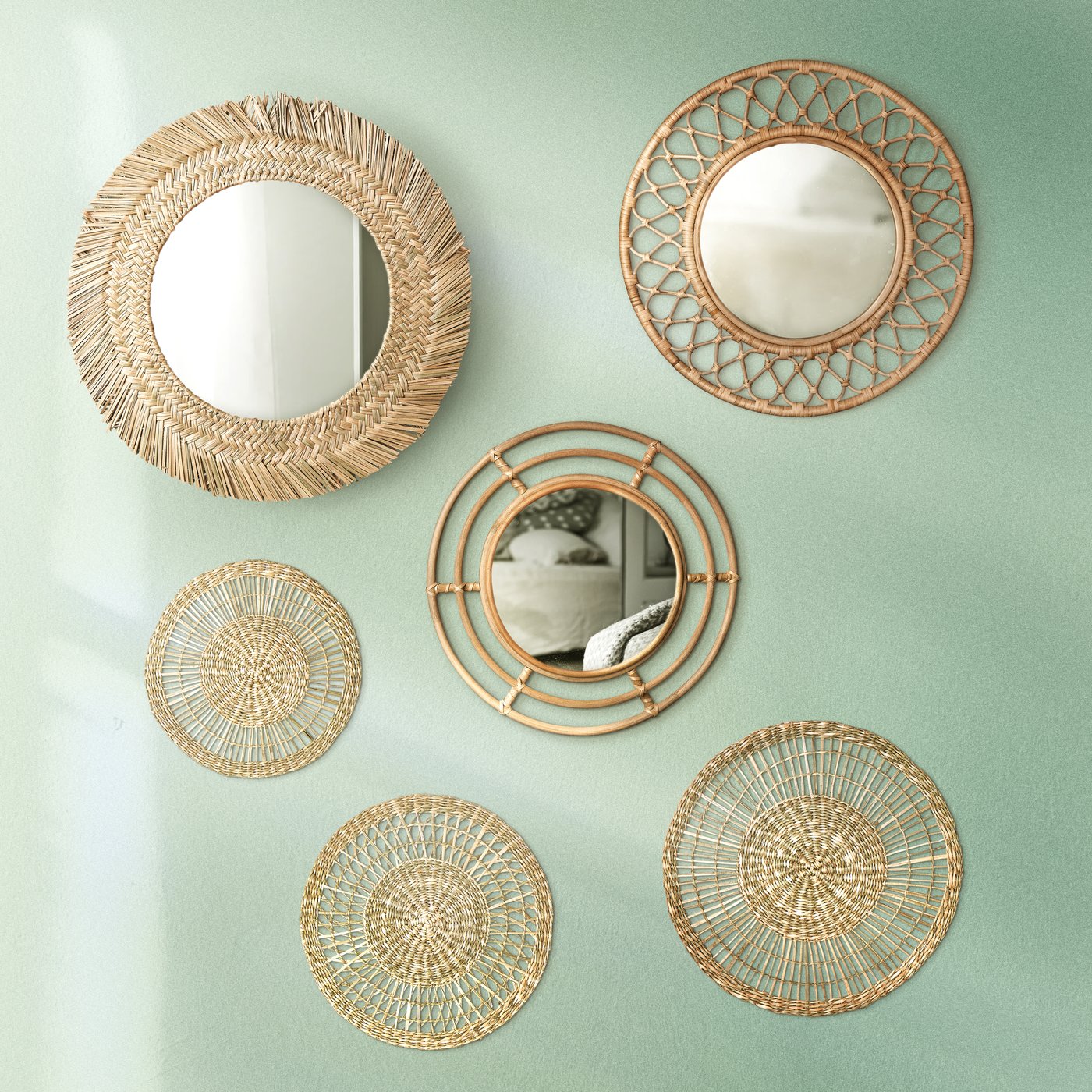 Plusieurs miroirs BUSKBO en rotin accrochés sur un mur vert pâle.