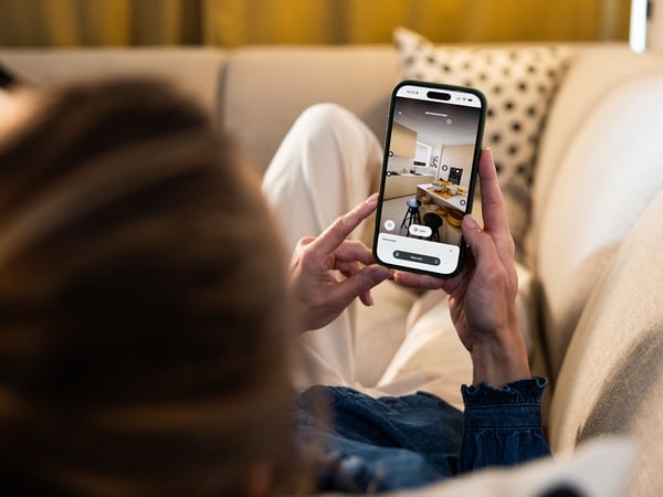 A woman laying in a sofa using the 3D kitchen tool on her smartphone.