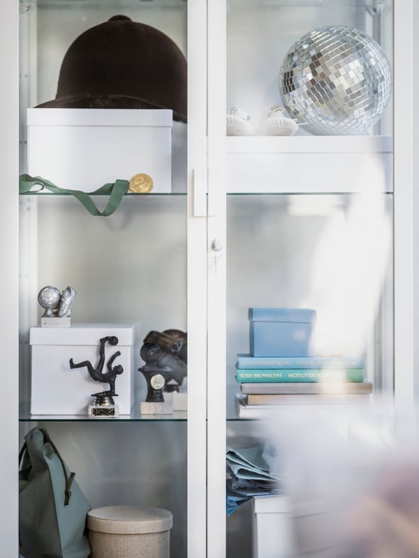 A display cabinet with a riding helmet, a disco globe, some boxes, books and smaller statues.