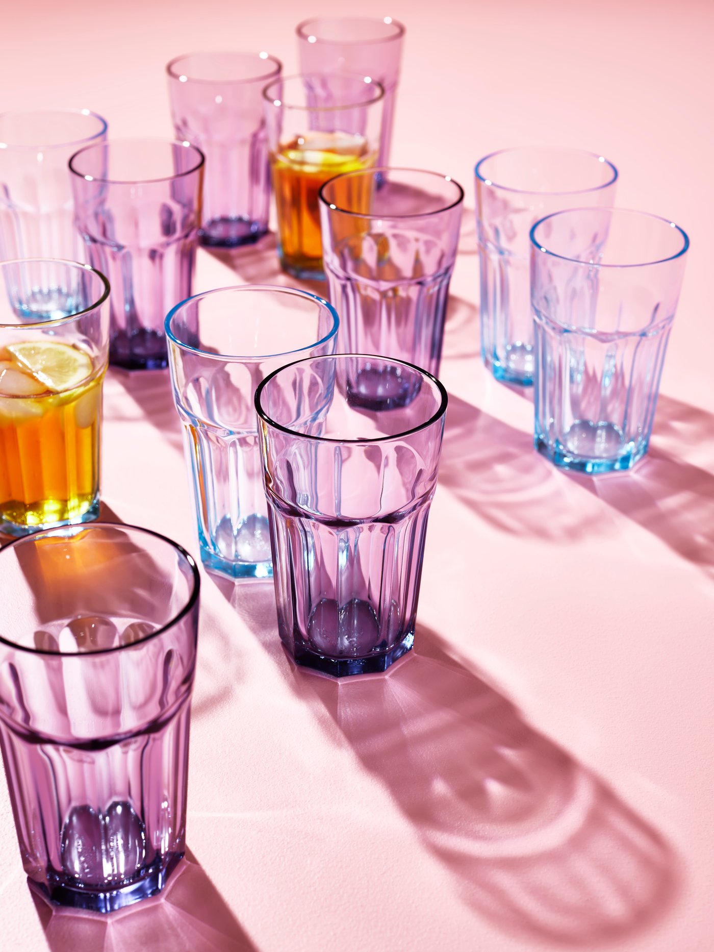 Cocina con varios vasos POKAL lila colocados junto a varios vasos POKAL azules, todos de vidrio templado.