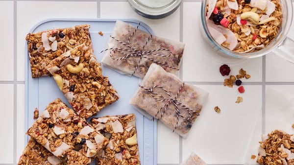 Home-made granola bars, cut into squares, some wrapped in baking paper, are placed on a grey chopping board on a table.