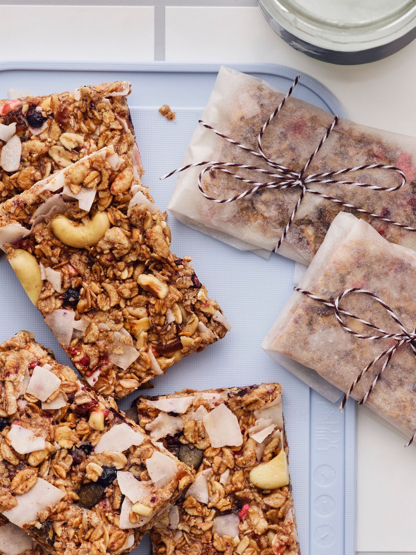 Selbstgemachte Müsliriegel, in Quadrate geschnitten, einige in Backpapier eingewickelt, liegen auf einem grauen Schneidebrett auf einem Tisch.
