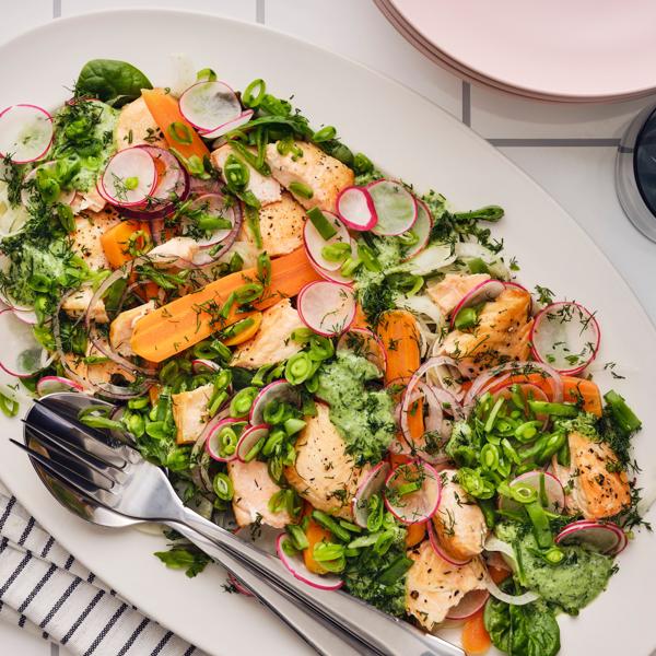 Ein bunter Salat mit gegrilltem Lachs, Radieschen, Karotten, Zuckerschoten und frischen Kräutern, der auf einem weißen Teller serviert wird.
