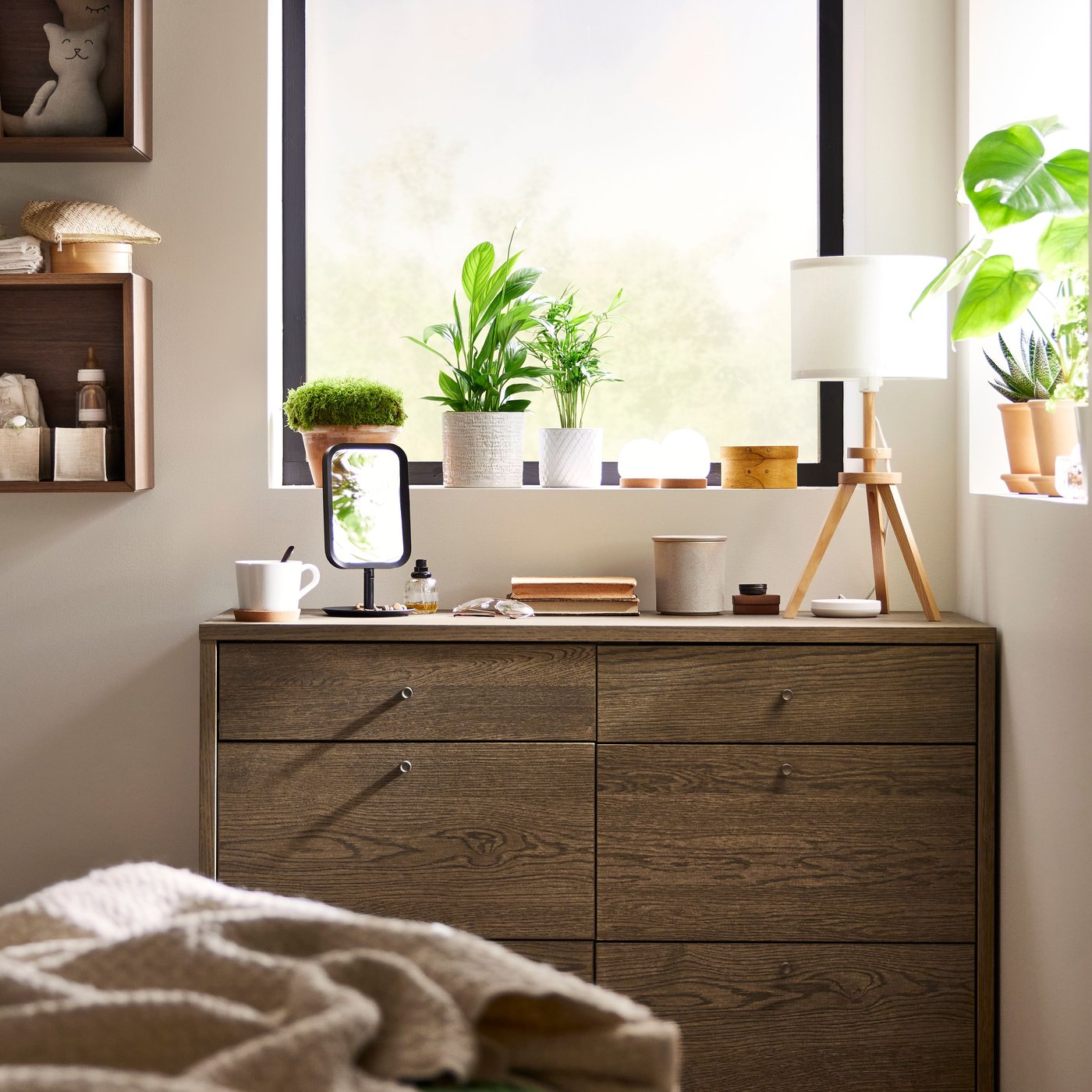 Eine TONSTAD Kommode mit 6 Schubladen aus braun gebeiztem Eichenfurnier, eine Tischlampe und andere Gegenstände darauf, in der Ecke eines Schlafzimmers.