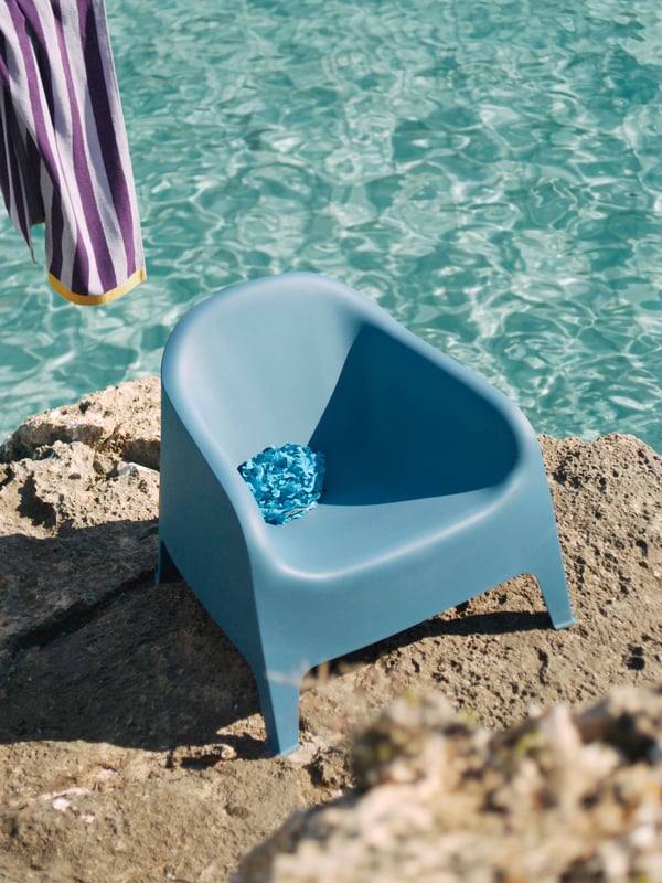 Ein blauer SKARPÖ Kunststoffsessel der für Draußen geeignet ist, steht auf einem Felsen am Meer. 