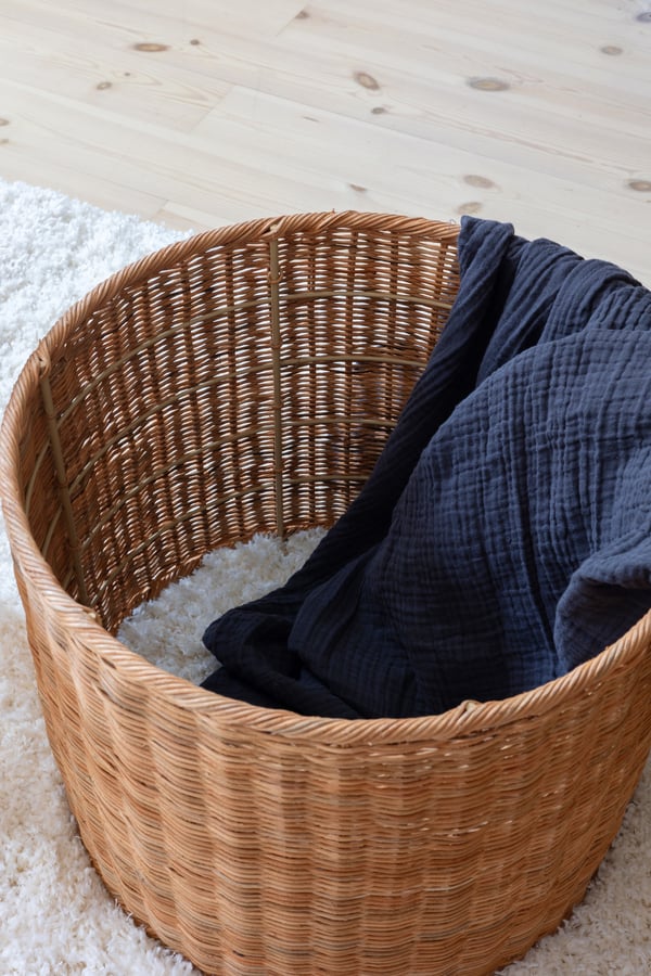 En rottingkurv med et blått pledd liggende oppi.