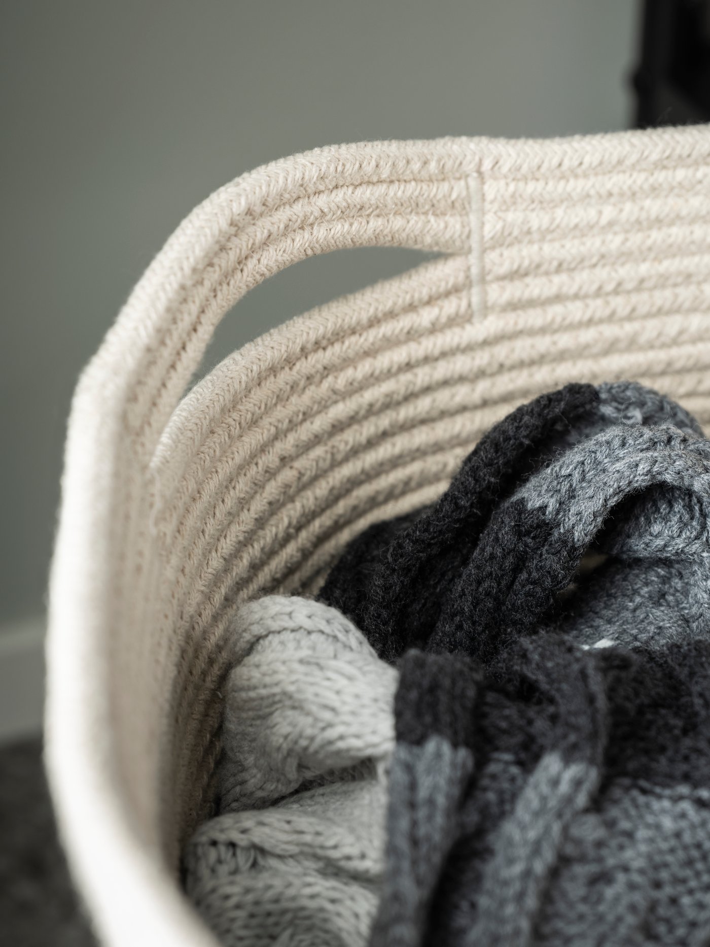 The handle and upper, natural-colour part of a TJABBIG textile basket, holding a bundle of knitted garments.