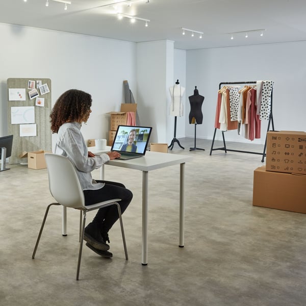 A person is having an online meeting in a half empty showroom with a clothing rack and moving boxes.