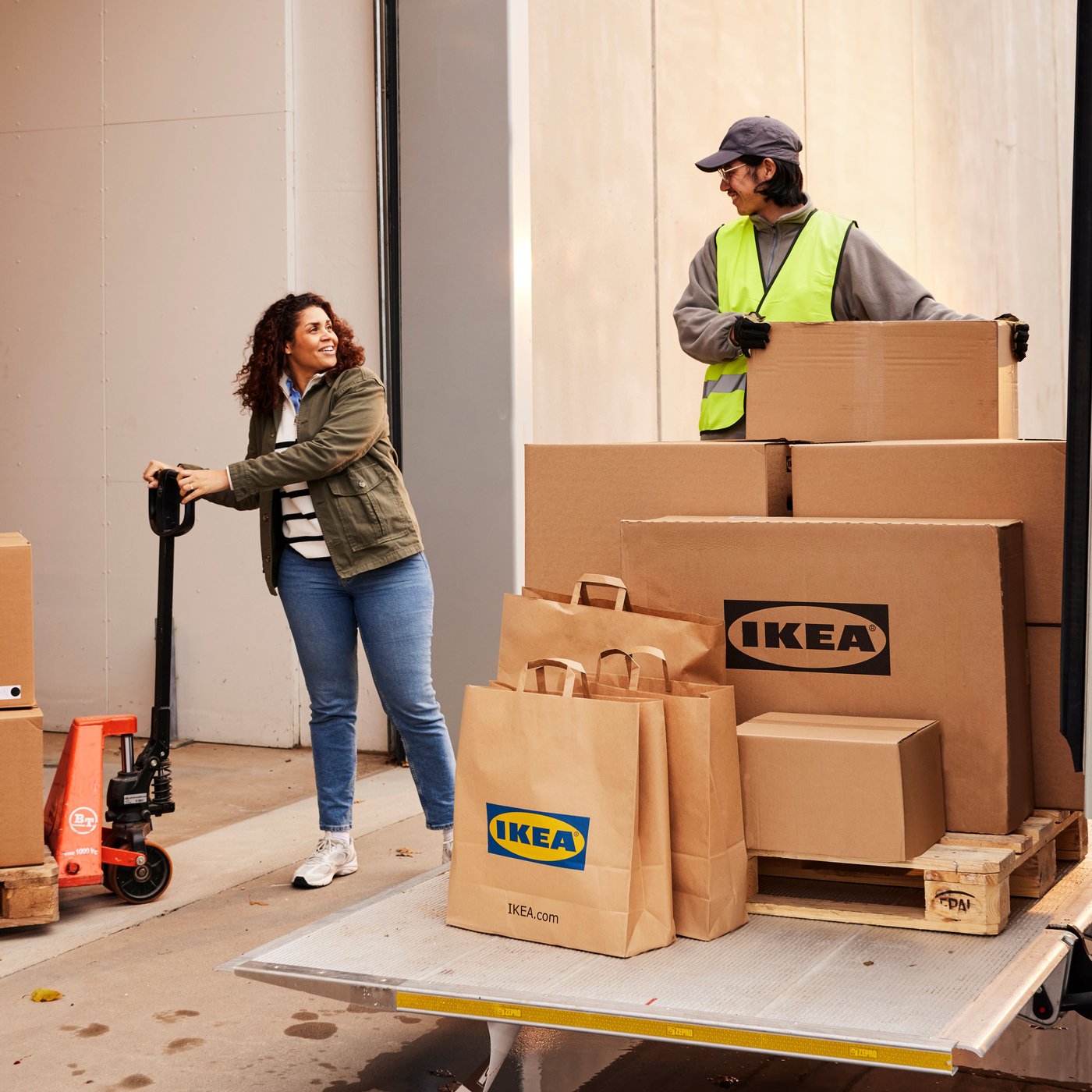 En smilende kunde holder en palleløfter med store IKEA-pakker og taler med chaufføren, der har flere pakker at losse.