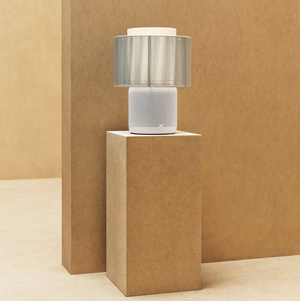 SYMFONISK bordslampa med wifi-högtalare i vitt/grått, placerad på ett sängbord.