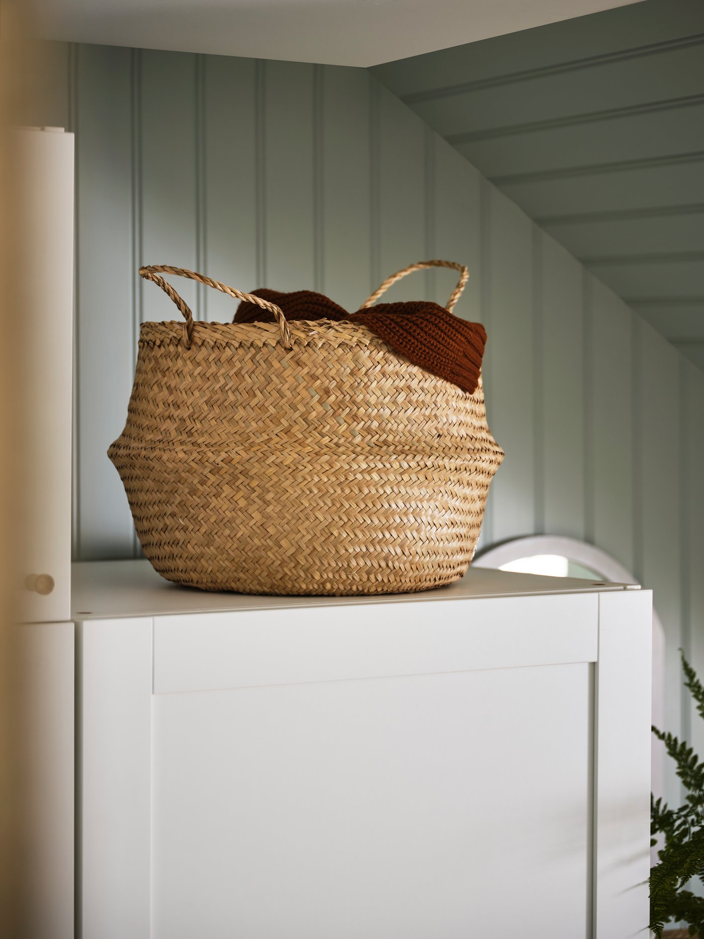 A braided FLÅDIS basket with a red textile inside sits on a white shelf.