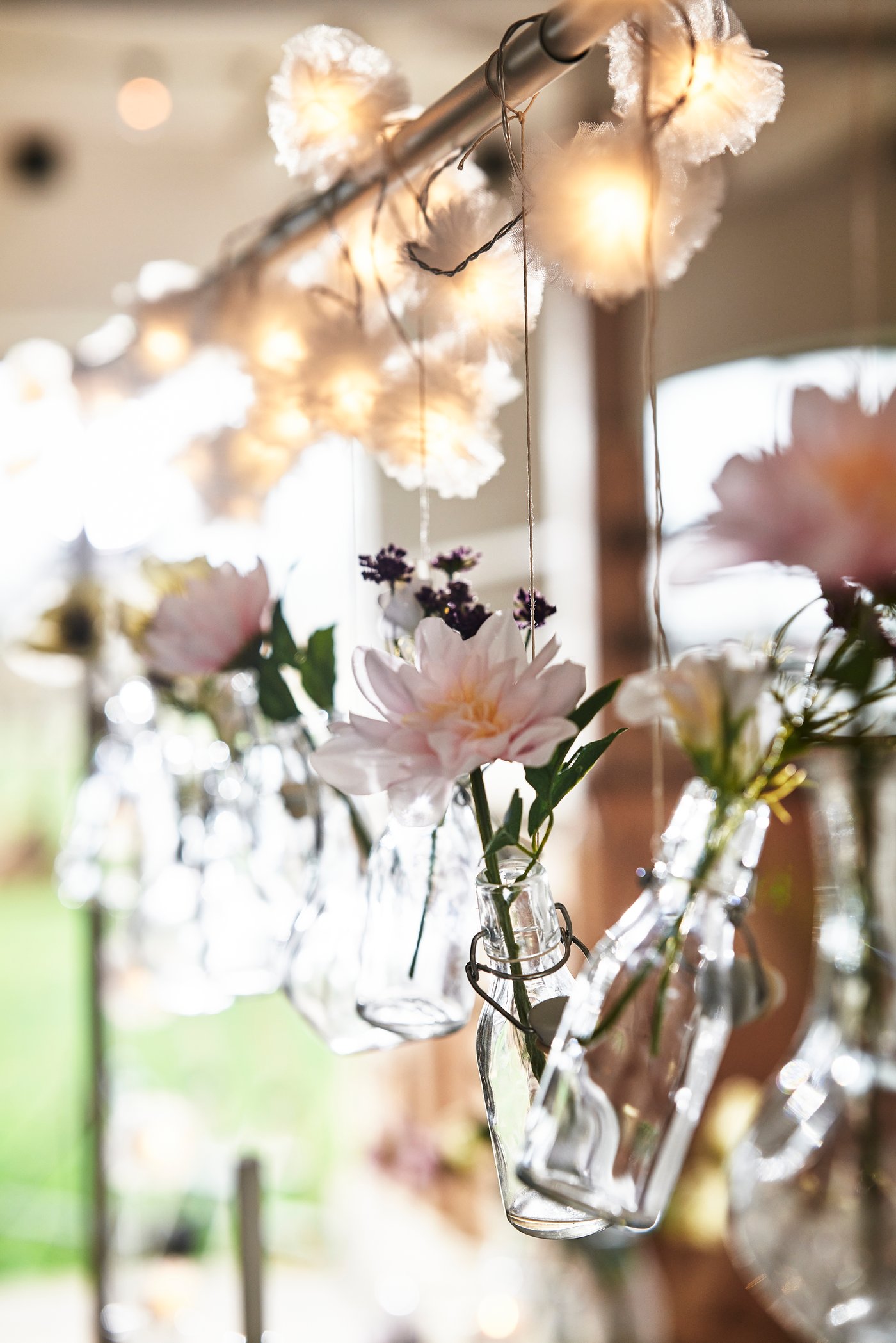 Ljusslingor och små glasvaser med blommor hängande i en stång över ett bord. 