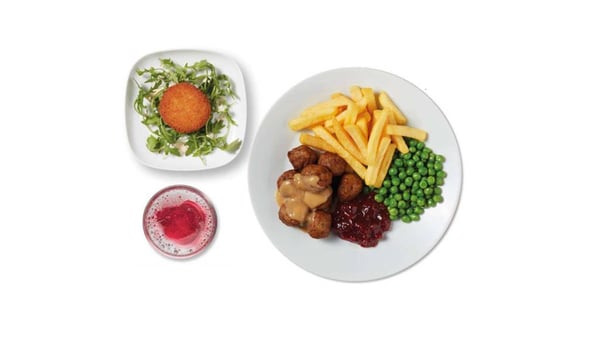 Assiette de boulettes avec sauce, frites, petits pois et confiture d’airelles, accompagnée d’une croquette sur un lit de salade et d’une boisson rouge.
