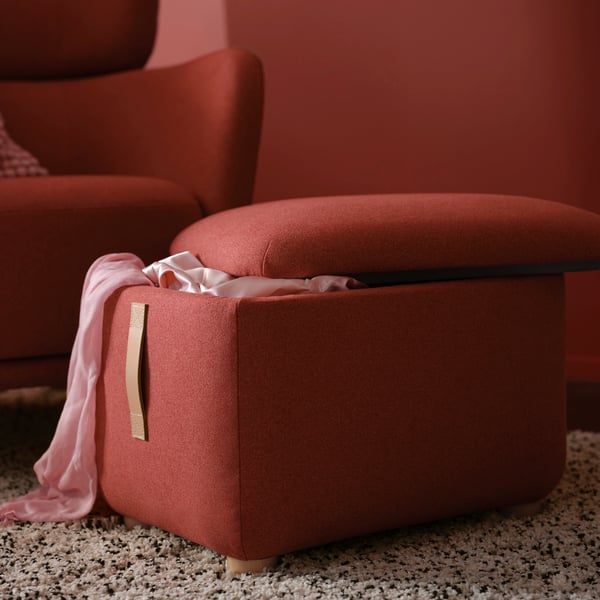 Roter Hocker mit Stauraum und passendem Sofasessel auf Teppich, rote Tapete im Hintergrund.