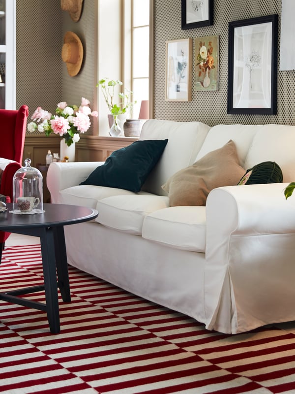 An EKTORP three-seat sofa in white is standing on a red and white rug in a living room that has a traditional look.