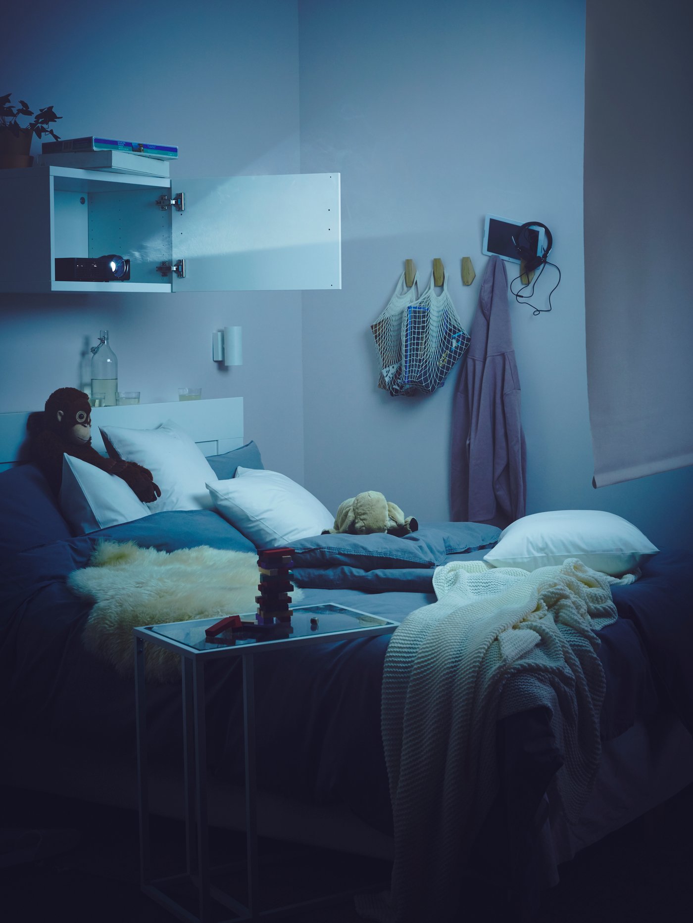 Dormitorio con estructura de cama con almacenaje y cabecero con manta y almohada ergonómica, y un estante encima.