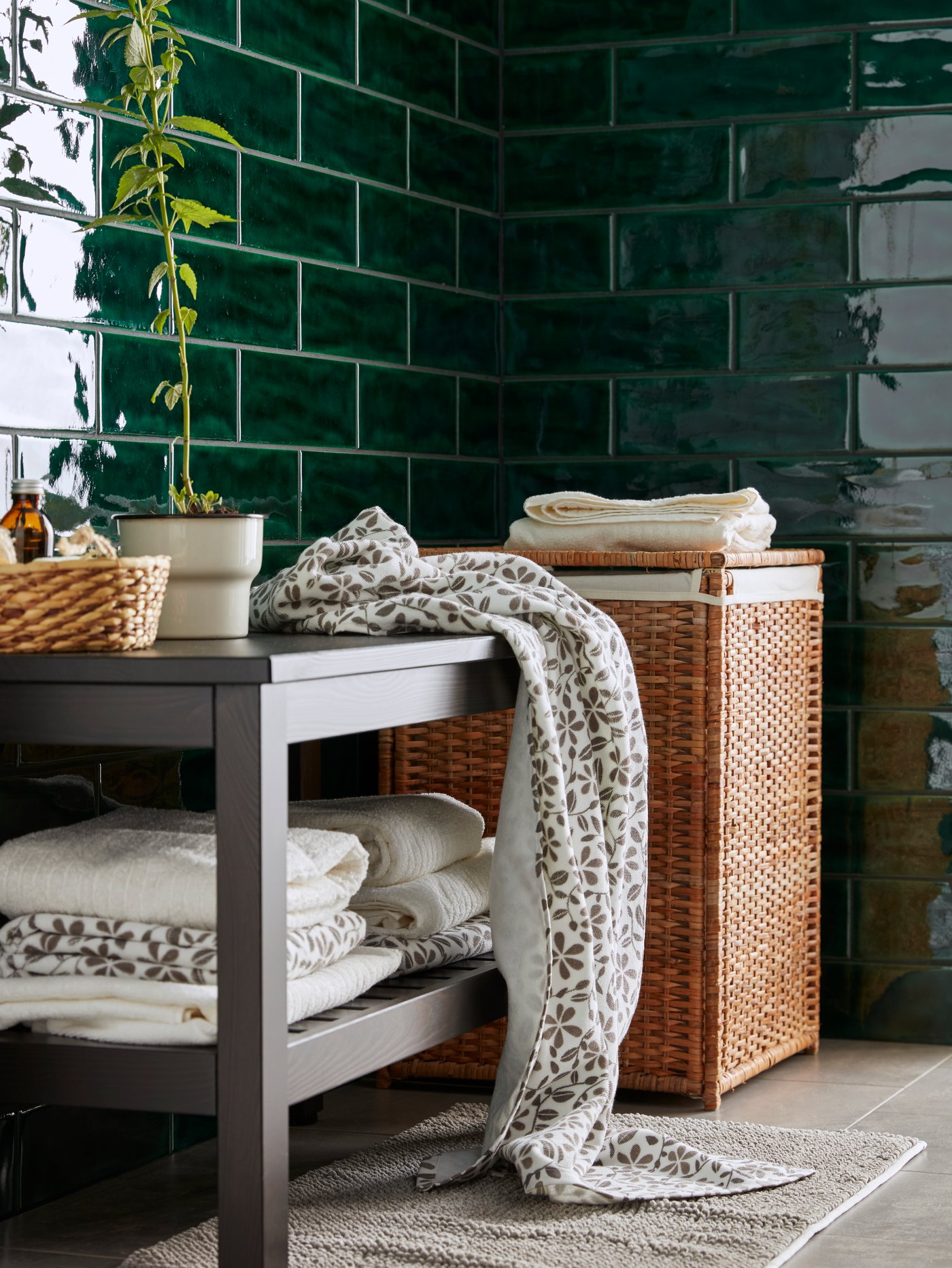 Dormitorio con cesto para la ropa sucia con forro, banco, toallas de baño, maceta, alfombrillas de baño, toallas de baño, plantas de interior y cajas con tapa.